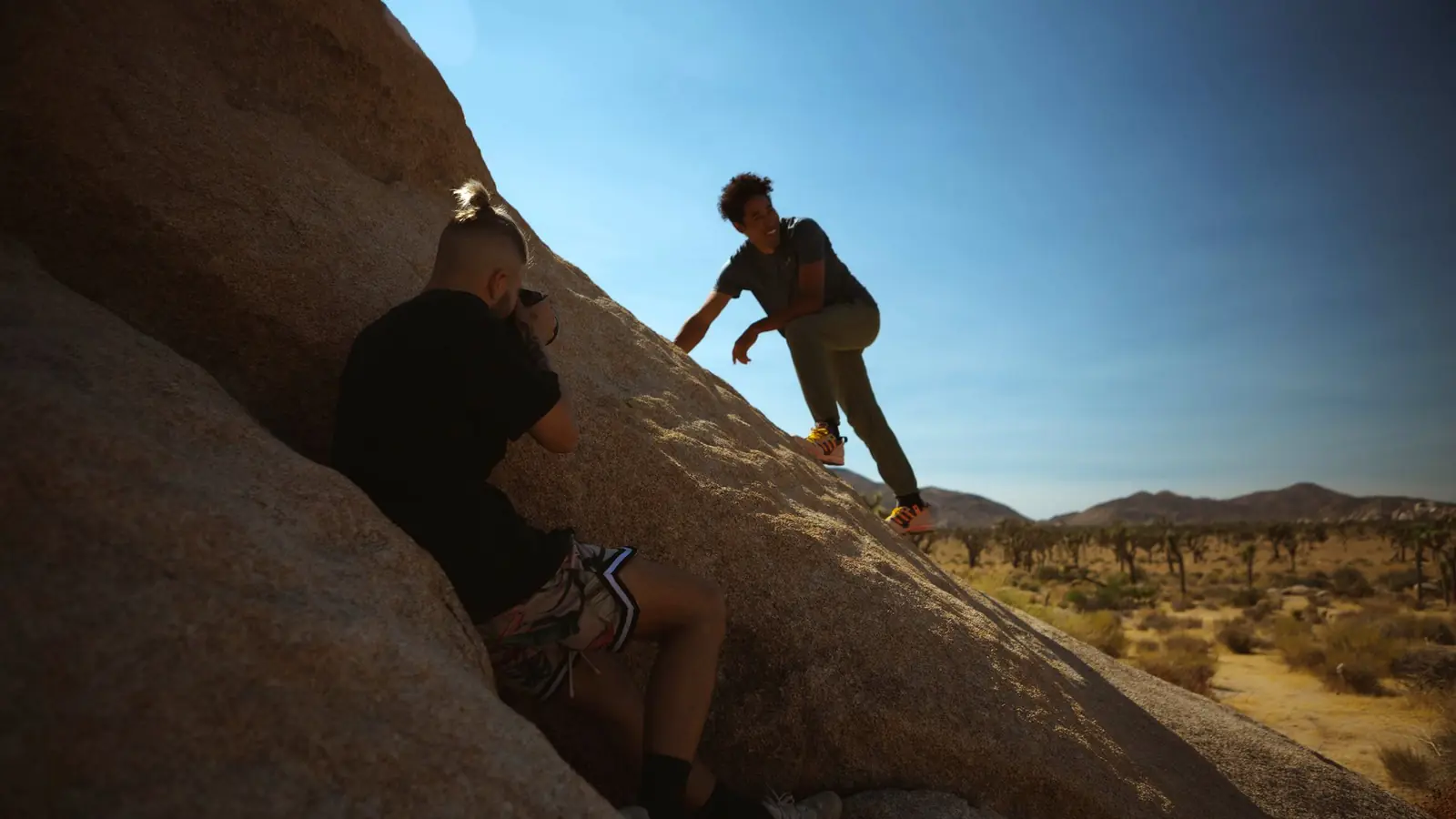 Two people scrambling up desert boulders at golden hour, behind the scenes on a MUUS shoot