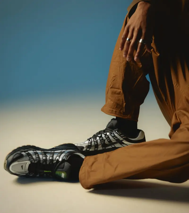 Black Nike sneakers and brown trousers against a blue backdrop