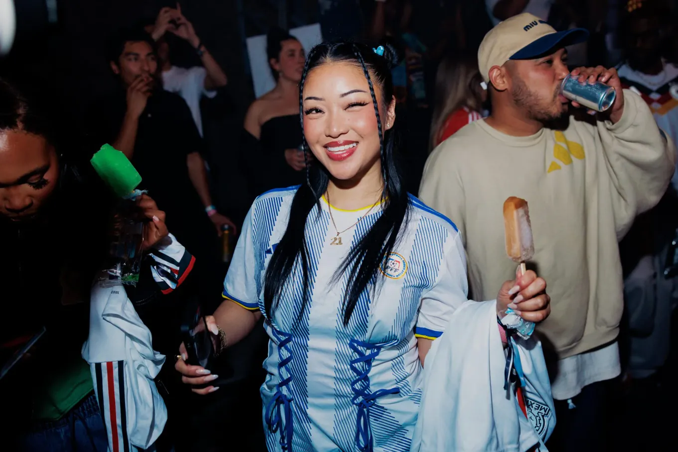 A crowd at a launch. A woman laughing to camera in a football shirt, friends either side of her