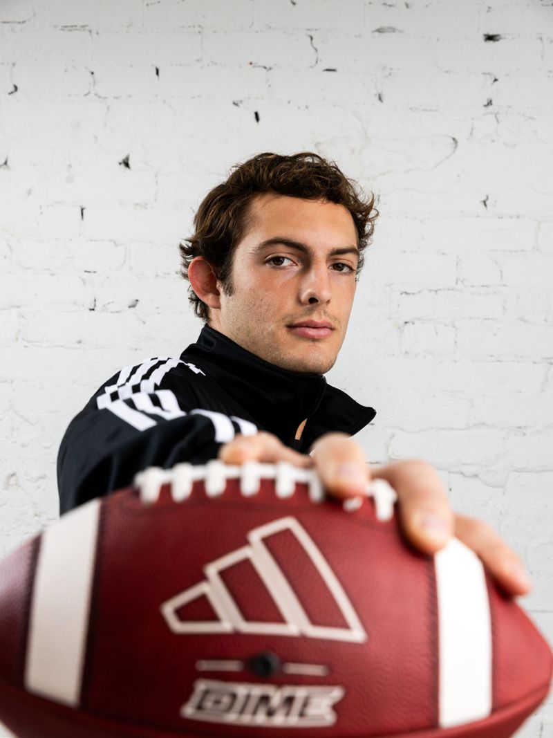 Charlie Becker holding an adidas football out to camera against a white brick wall