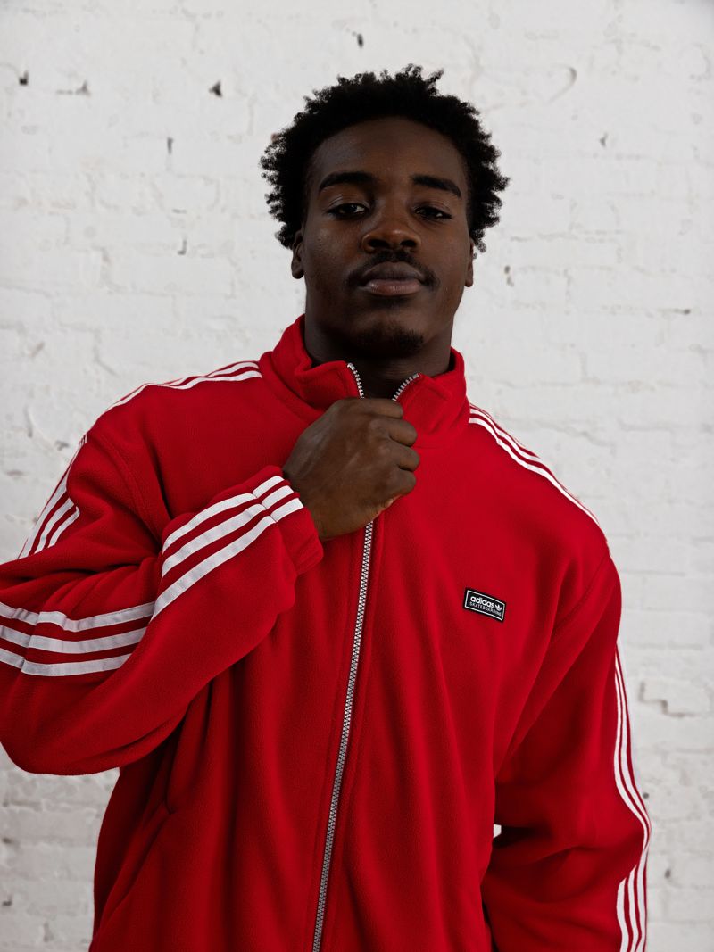 Nick Marsh in a red adidas track jacket, waist up, against white brick