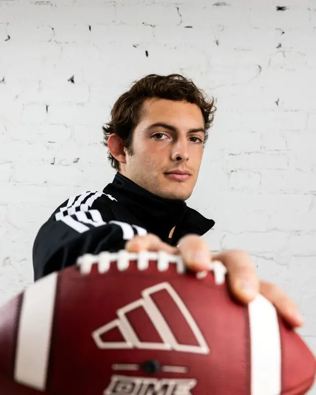An Indiana football player holding the ball to camera in an adidas jacket